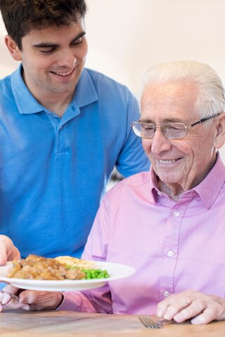 Pflegekraft serviert einem Senior das Mittagessen am Tisch @ 